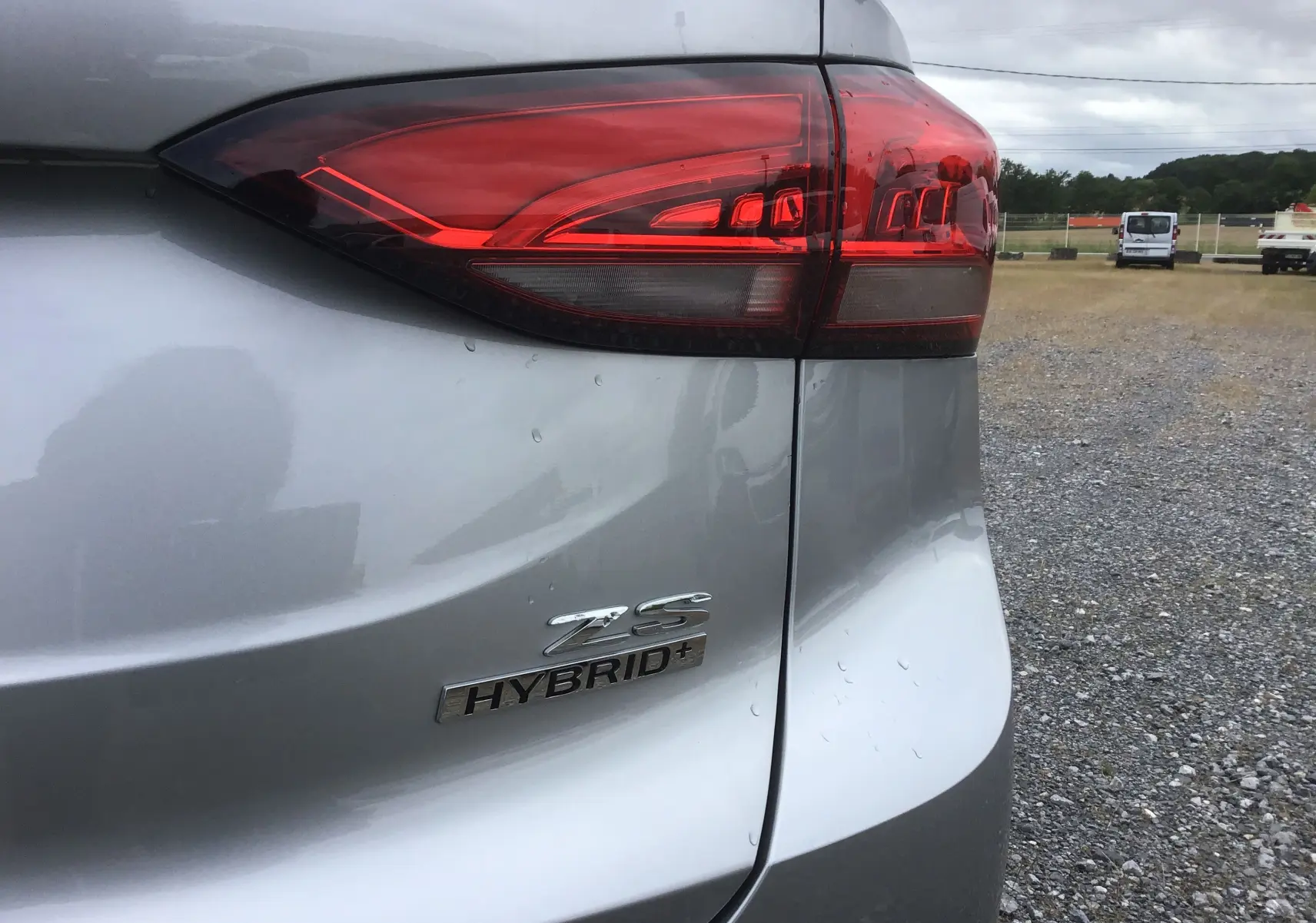 Gros plan sur le feu arrière droit et le logo Hybrid+ du MG ZS Cosmic Silver, vue arrière côté droit.
