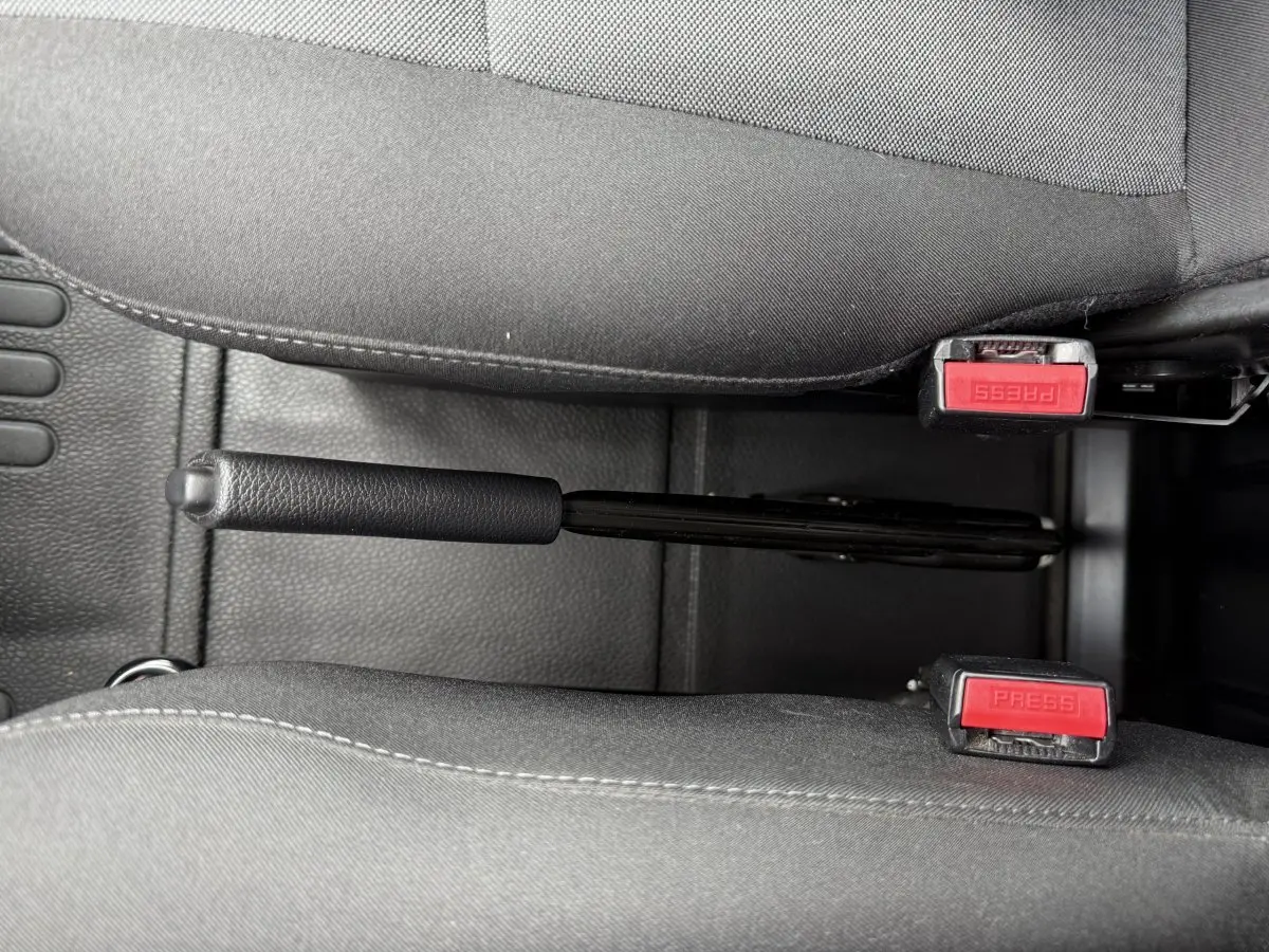Vue rapprochée de la poignée de frein à main noire entre deux sièges gris dans l'habitacle du Renault Master blanc.