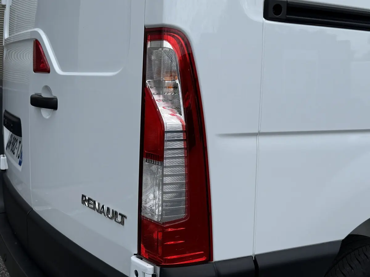 Vue arrière droite d’un Renault Master blanc, mettant en valeur le feu arrière vertical et le logo Renault sur la porte.