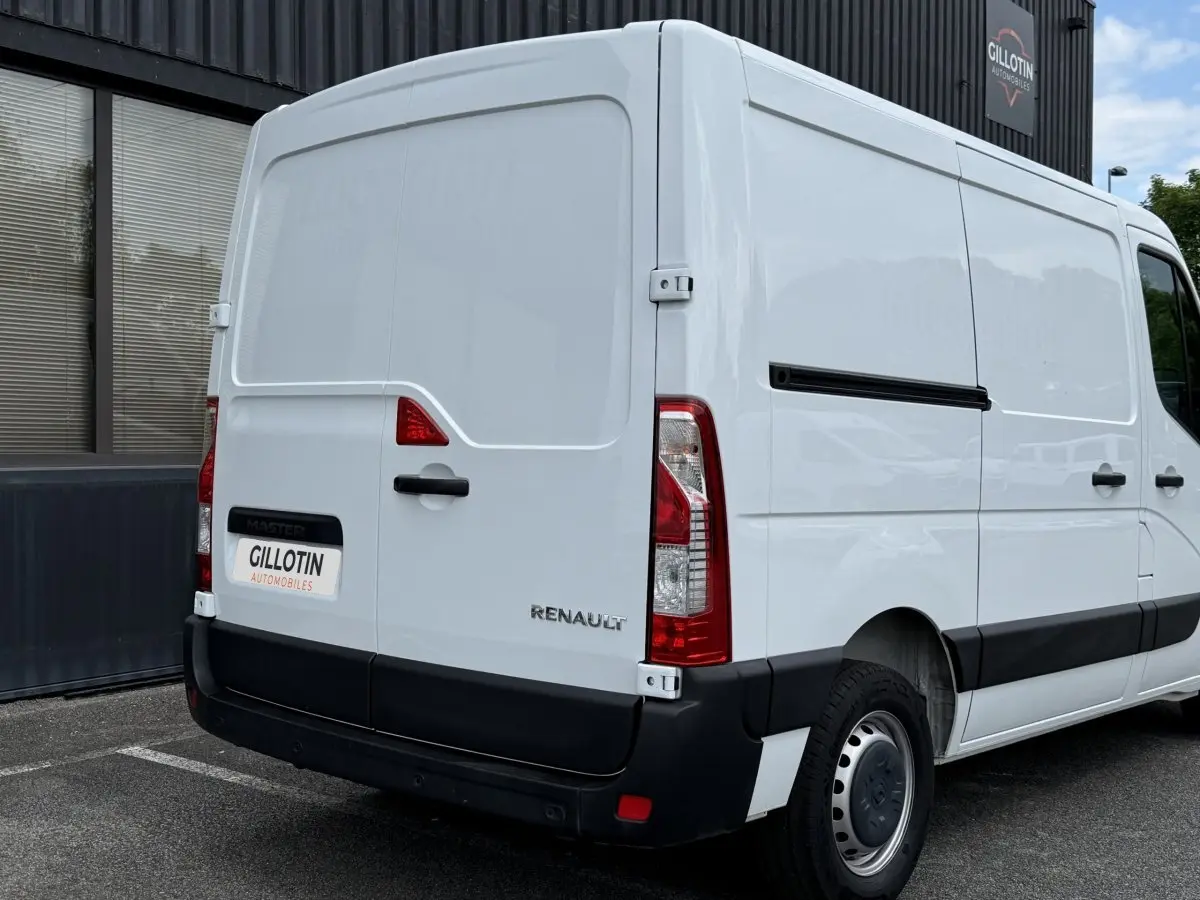 Vue 3/4 arrière droite d’un utilitaire Renault Master blanc avec porte latérale coulissante et feux arrière verticaux.