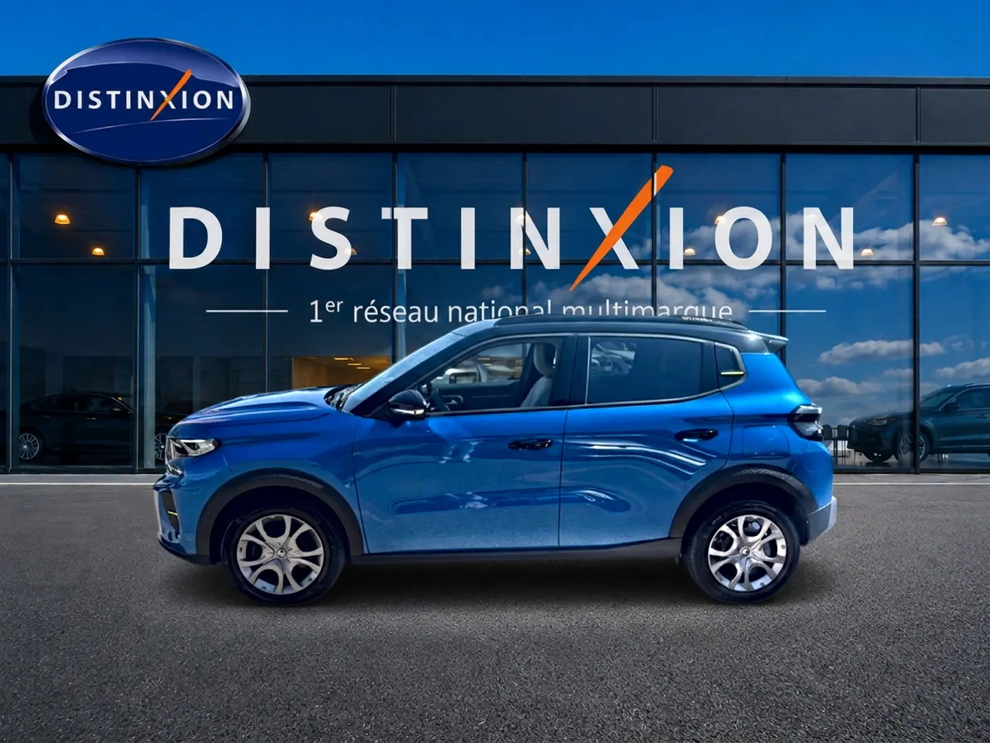 Profil latéral droit d'une Citroën C3 2025 bleu, avec jantes alu et toit noir devant une vitrine Distinxion.