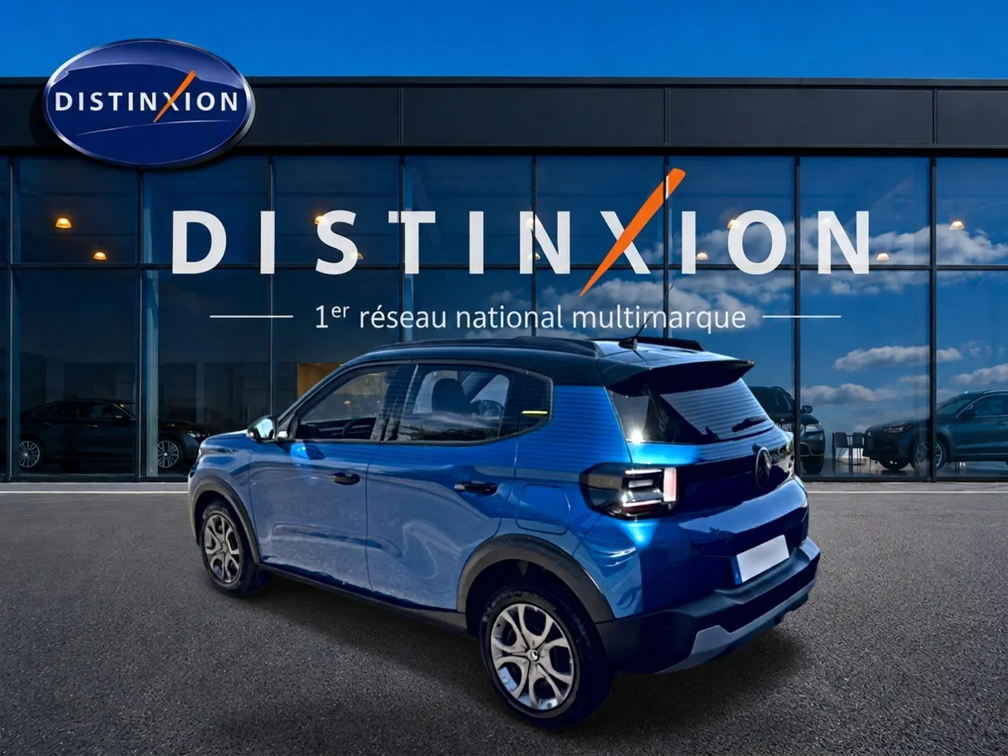 Vue 3/4 arrière droite d'une Citroën C3 2025 bleu avec toit noir et jantes alu devant une vitrine Distinxion.
