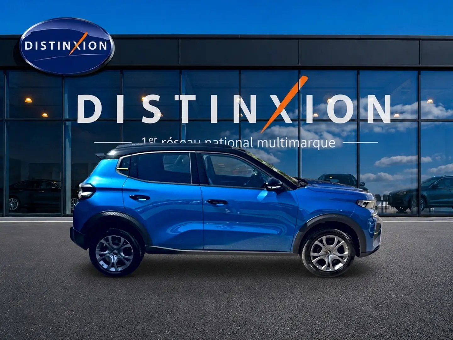 Profil droit d'une Citroën C3 bleu 2025 avec jantes alu, garée devant une vitrine Distinxion.