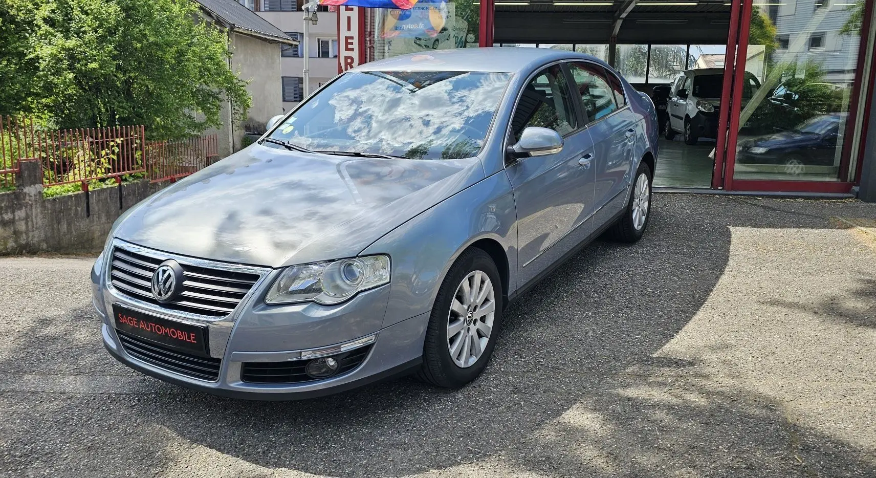 Volkswagen Passat 1.4 TSI bleu vue 3/4 avant droit, stationnée devant un garage avec plaque Sage Automobile.