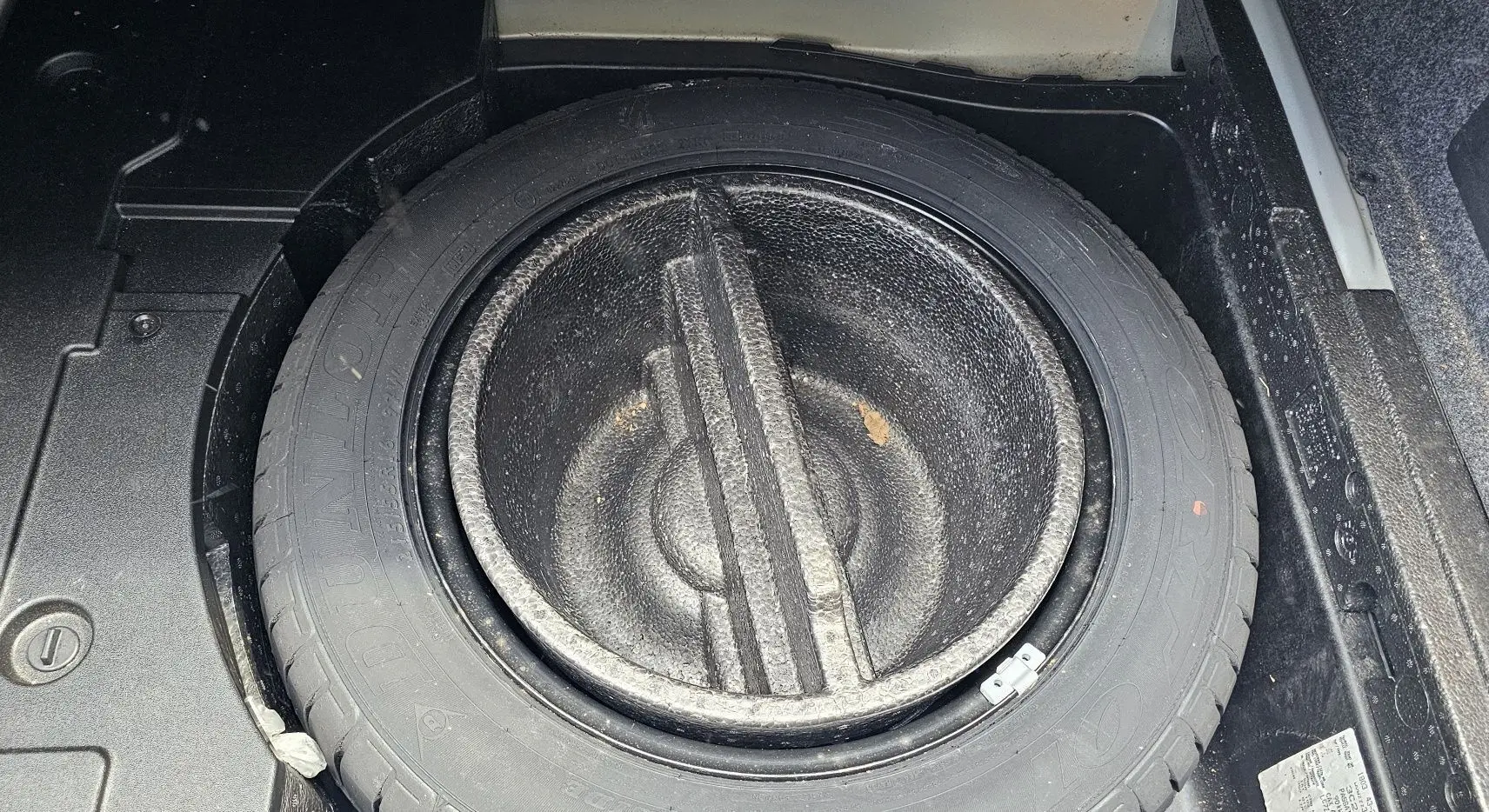 Gros plan sur la roue de secours et son logement dans le coffre d'une Volkswagen Passat bleue de 2009.