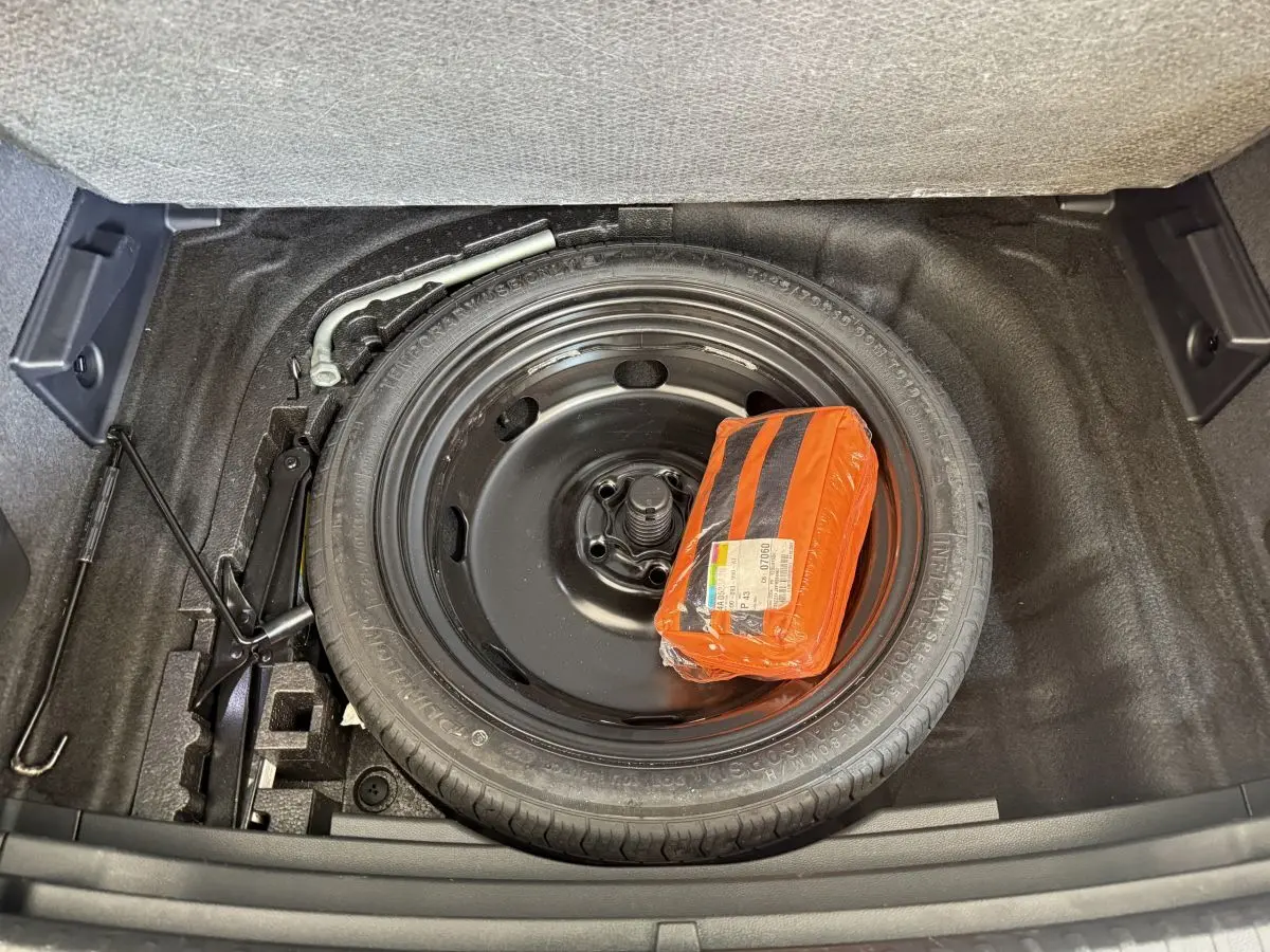 Vue plongeante sur la roue de secours noire et le kit de sécurité orange dans le coffre du SEAT Ateca gris clair.
