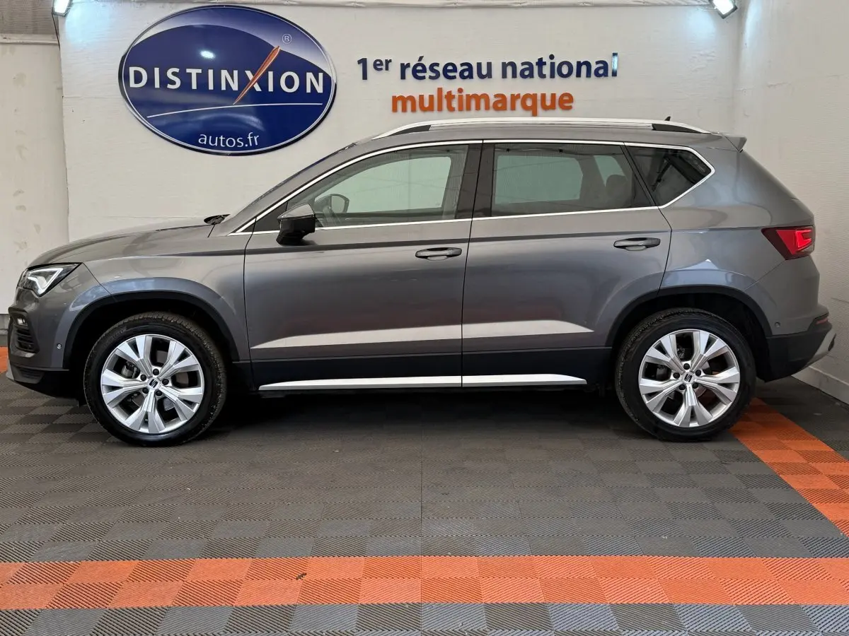 Profil côté gauche d'un SUV SEAT Ateca gris clair 2023 avec jantes alliage et barres de toit chromées.