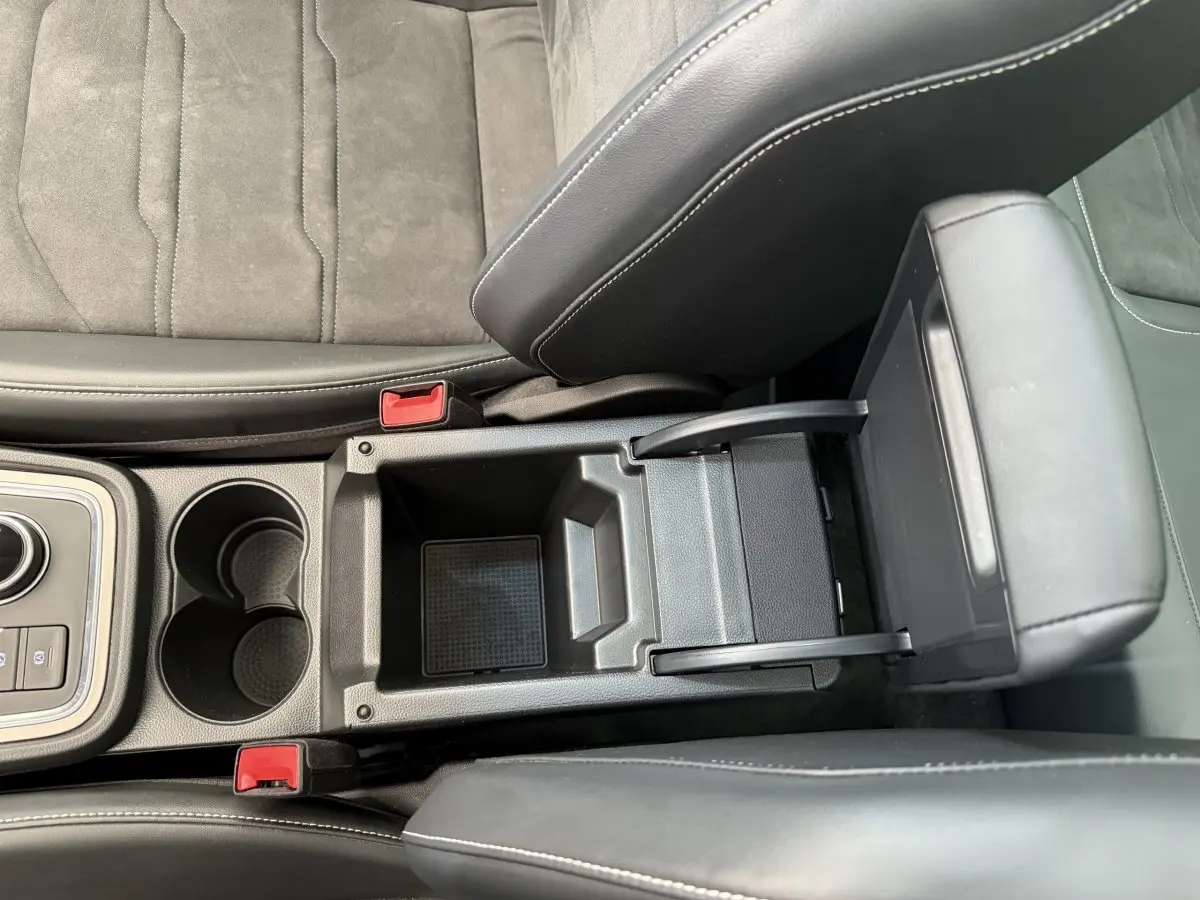 Vue plongeante sur l'accoudoir central noir ouvert et les porte-gobelets entre les sièges gris clair du SEAT Ateca 2023.
