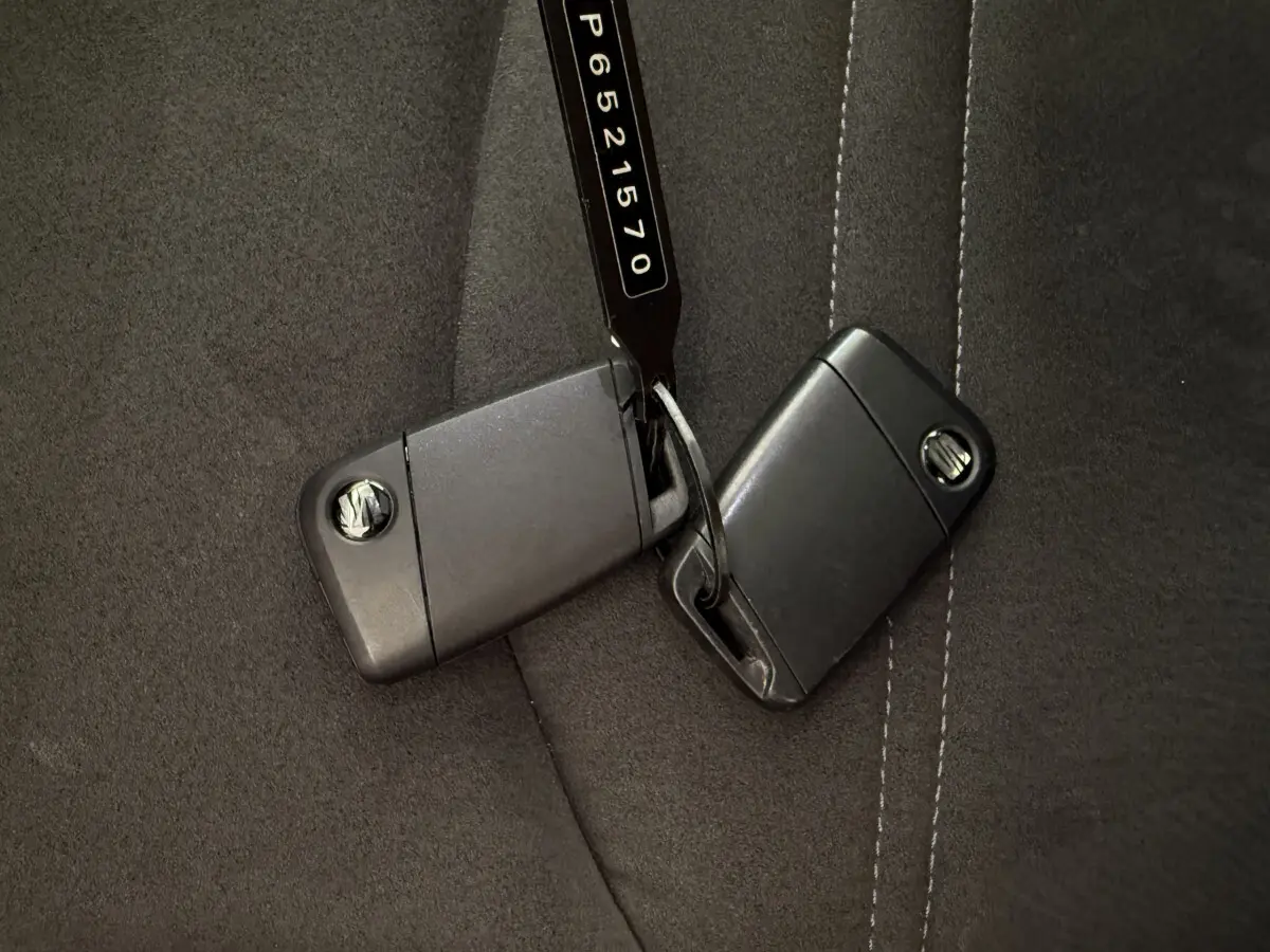 Gros plan sur deux clés noires SEAT posées sur un siège en tissu gris foncé avec surpiqûres blanches.