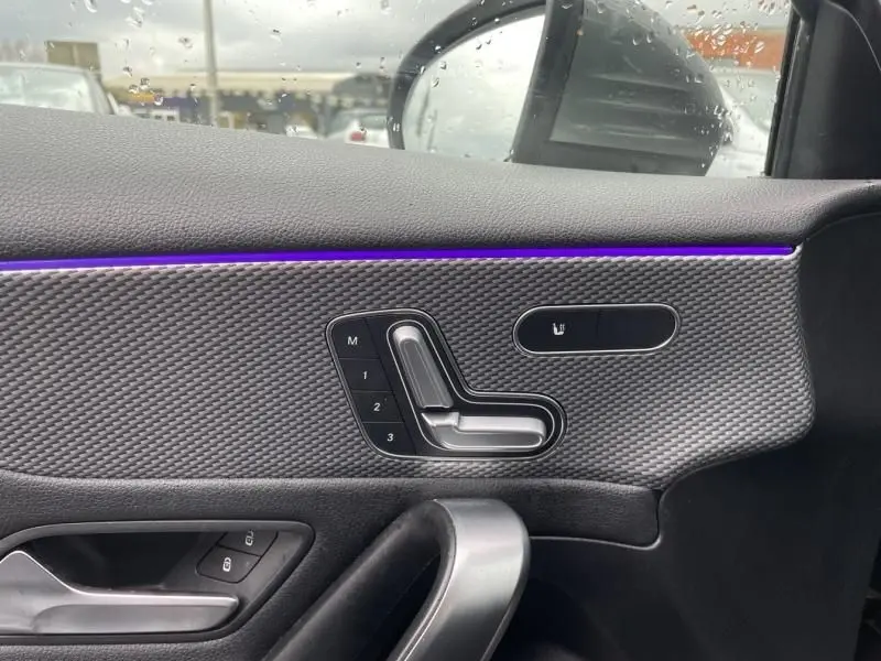 Détail intérieur côté gauche de la porte d’une Mercedes Classe A 2019 gris foncé, avec commandes de siège et éclairage d’ambiance violet.