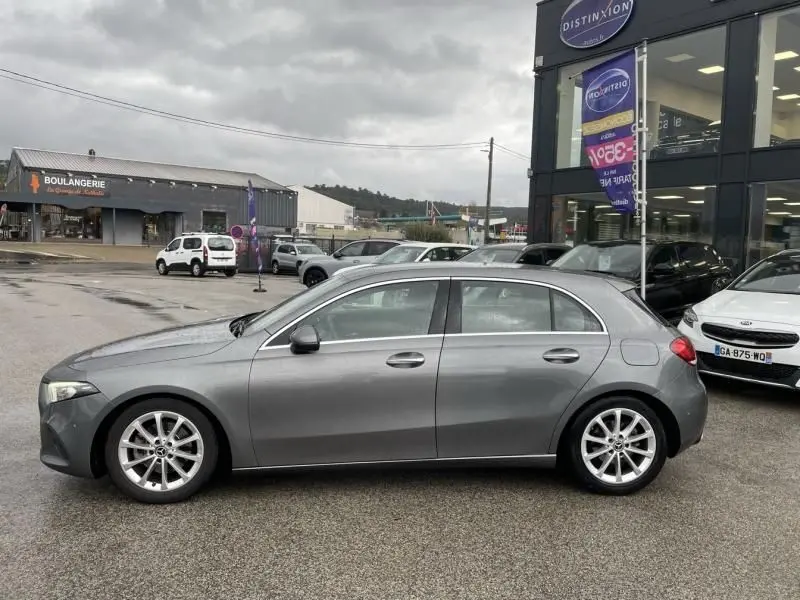 Vue de profil côté gauche d'une Mercedes Classe A 200 gris foncé métal garée devant un concessionnaire par temps couvert.
