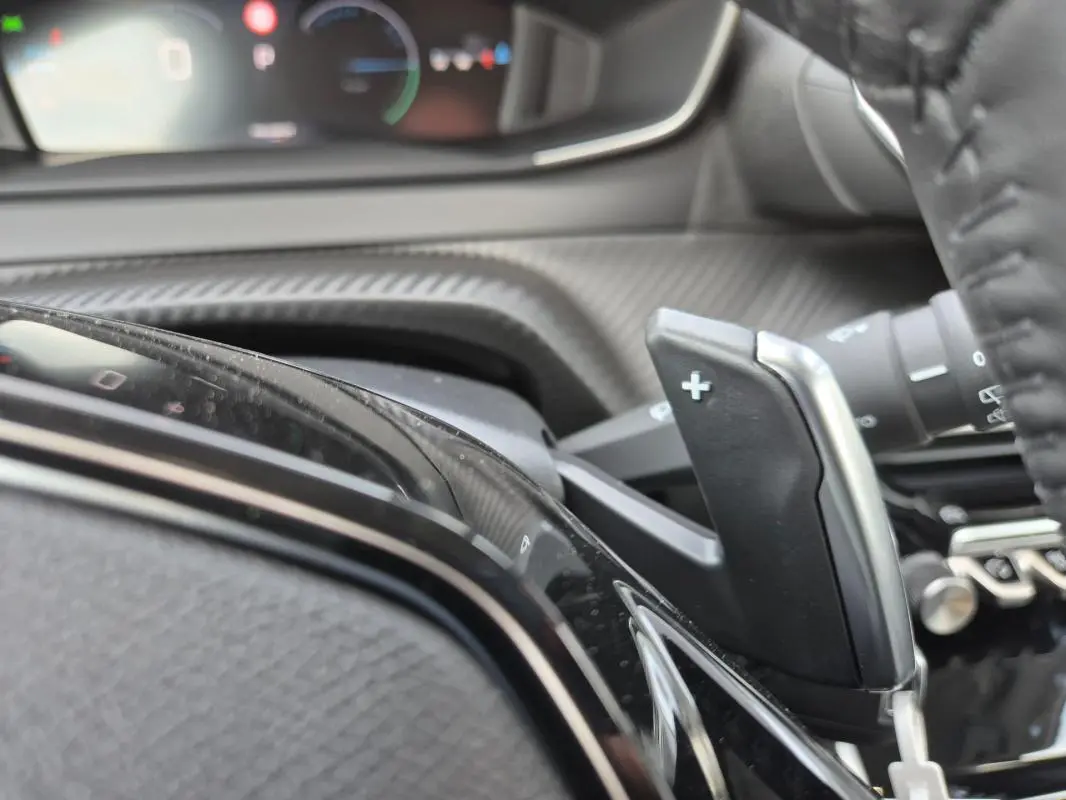 Gros plan sur la palette de changement de vitesse "+" côté droit du volant dans l'habitacle d'une Peugeot 208 blanche 2025.