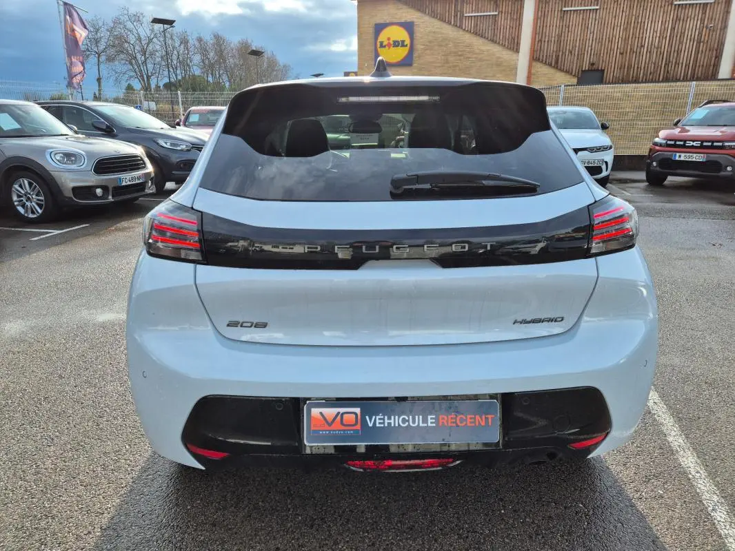 Vue arrière d'une Peugeot 208 Hybrid blanche de 2025 avec feux LED et logo Peugeot noir brillant.