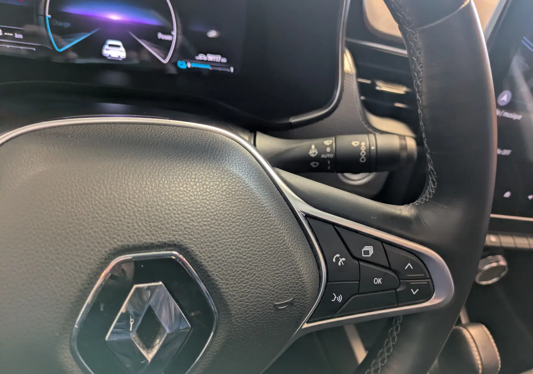 Gros plan sur le volant cuir noir du Renault Arkana 2023, avec commandes intégrées et tableau de bord numérique en arrière-plan.