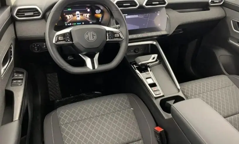 Vue intérieure du poste de conduite du MG ZS Pebble Black 2025, avec volant multifonction, écran tactile et sièges en tissu noir.
