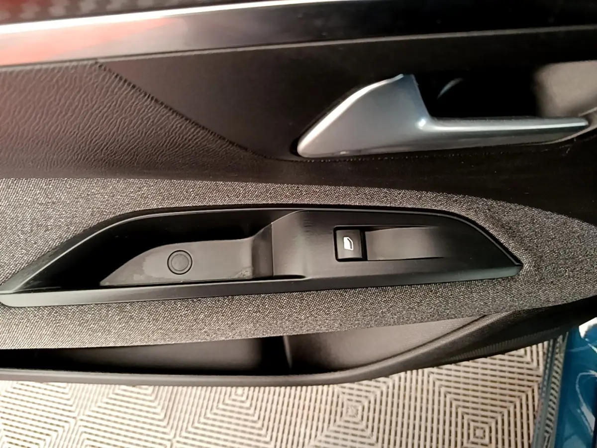 Détail de la poignée intérieure côté conducteur du Peugeot 5008 bleu, avec bouton de verrouillage et garniture textile grise.