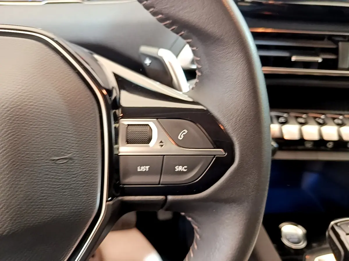 Gros plan sur le volant cuir multifonctions côté gauche du Peugeot 5008 bleu, avec commandes intégrées et tableau de bord en arrière-plan.