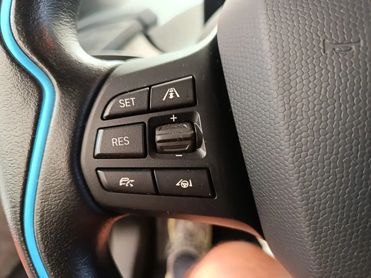 Gros plan sur les commandes de régulateur de vitesse au volant cuir noir avec surpiqûre bleue d'une BMW i3 120 Ah Atelier.