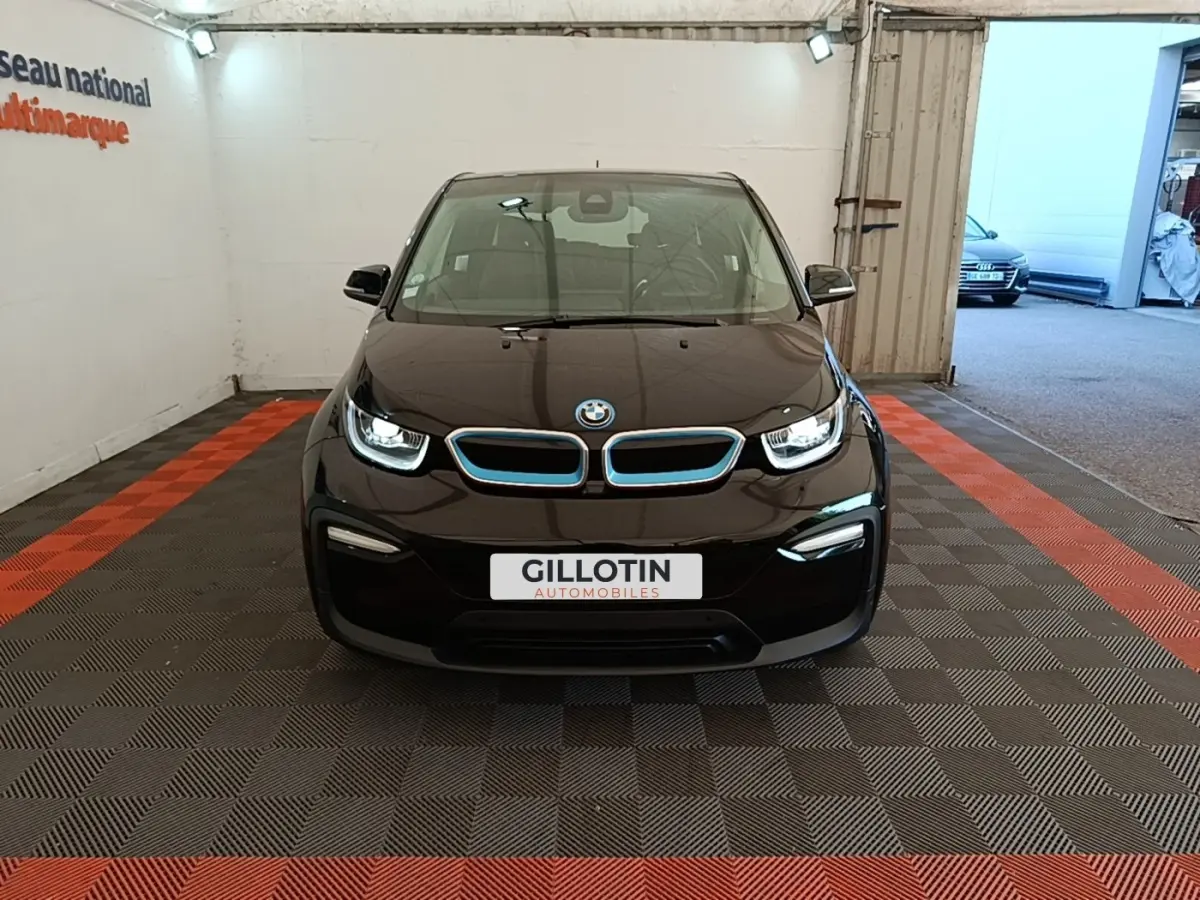 BMW i3 120 Ah Atelier noire vue de face, avec calandre bleutée et phares LED allumés en intérieur showroom.