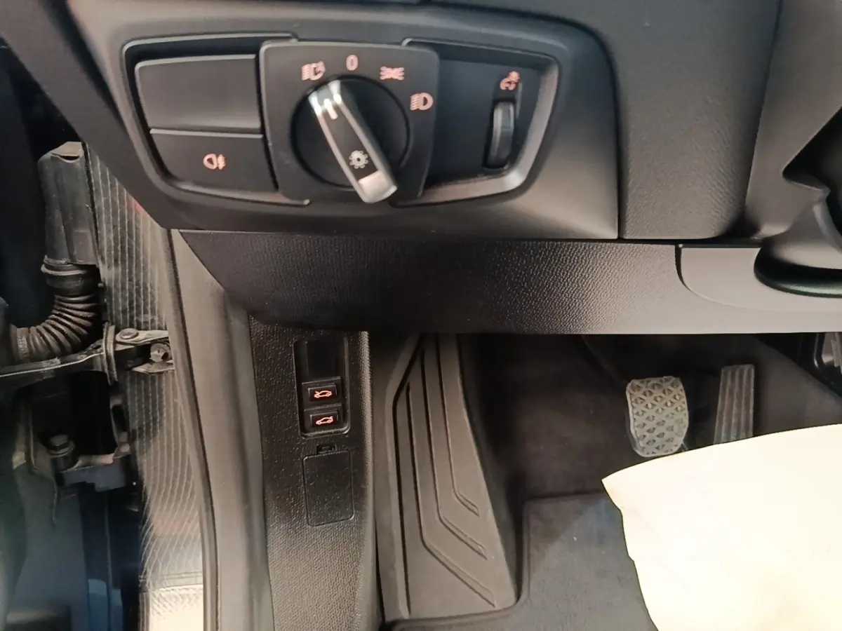 Vue intérieure côté gauche du poste de conduite d'une BMW i3 noire, avec commandes d'éclairage et pédales visibles.