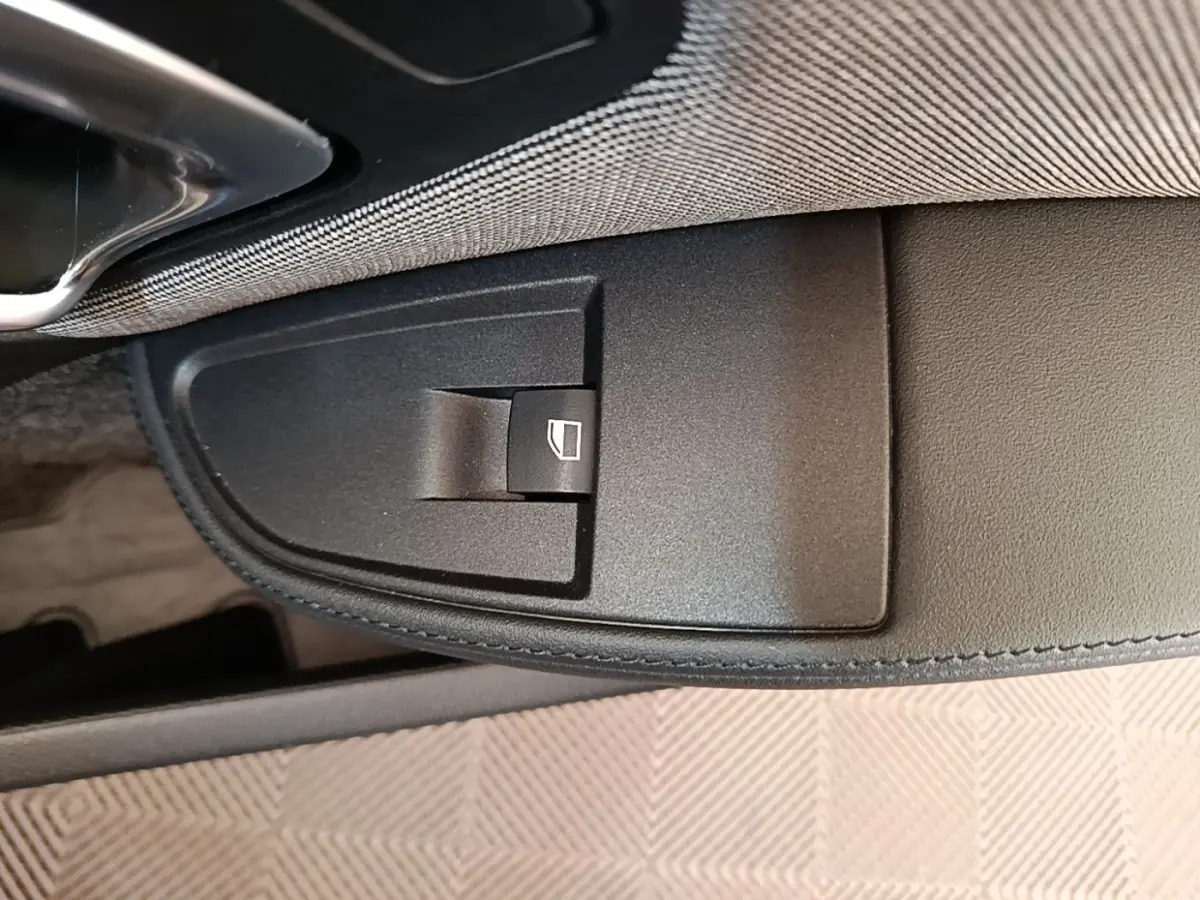 Gros plan sur le bouton de commande de lève-vitre côté conducteur dans l'intérieur noir de la BMW i3 120 Ah Atelier.