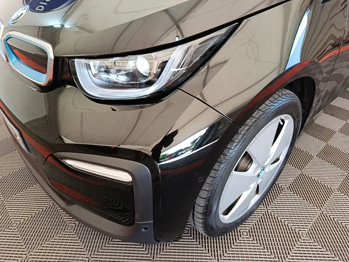 Gros plan sur l'avant droit noir d'une BMW i3 120 Ah Atelier, mettant en valeur le phare LED et la jante spécifique.