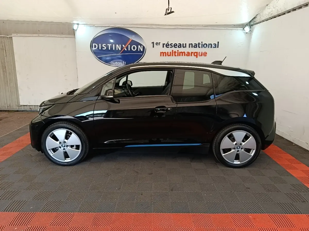 Profil côté gauche de la BMW i3 120 Ah Atelier noire, avec ses jantes distinctives et toit contrastant en intérieur fermé.