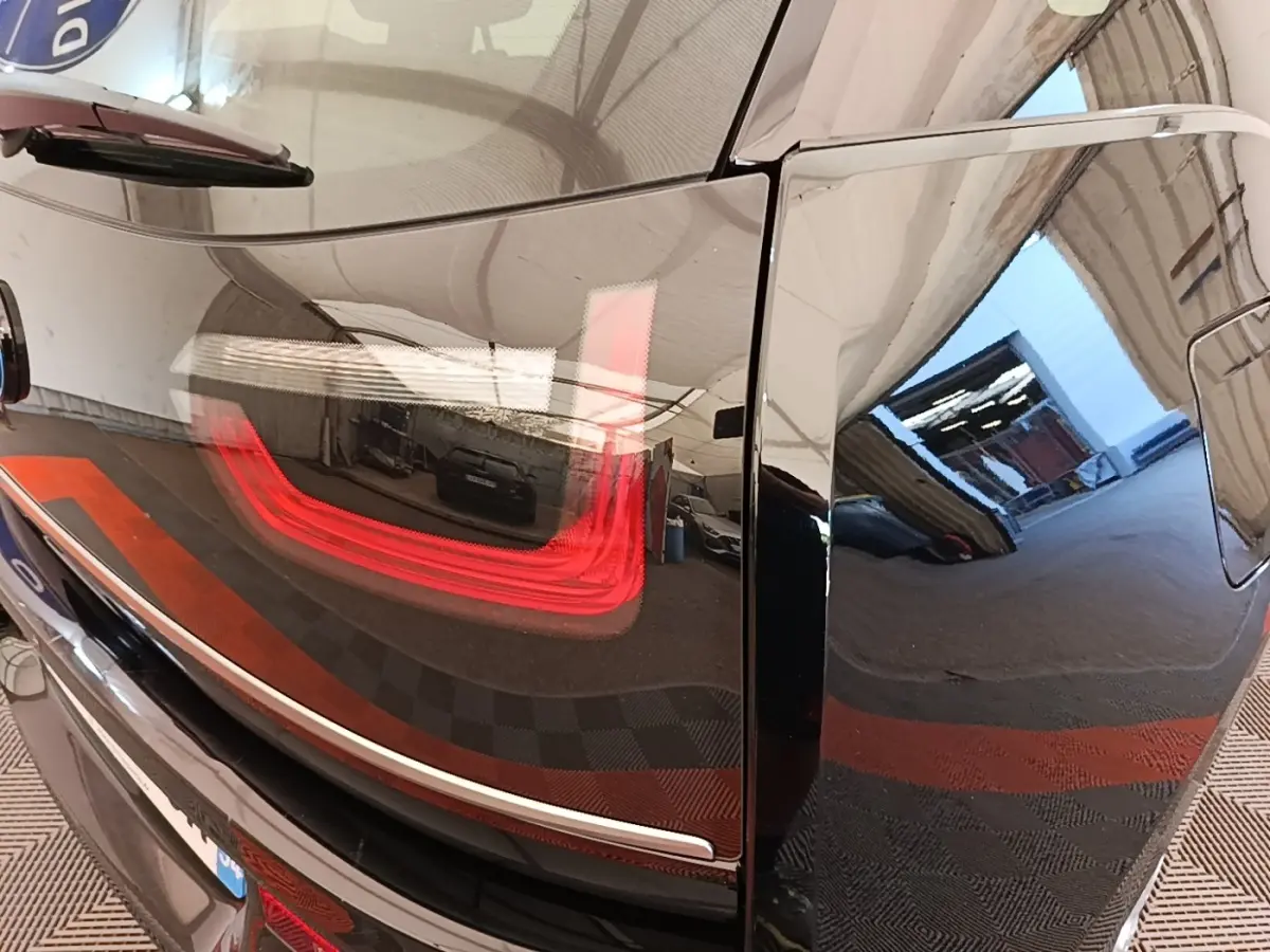 Gros plan sur le feu arrière gauche rouge d’une BMW i3 noire, reflétant l’intérieur d’un garage.