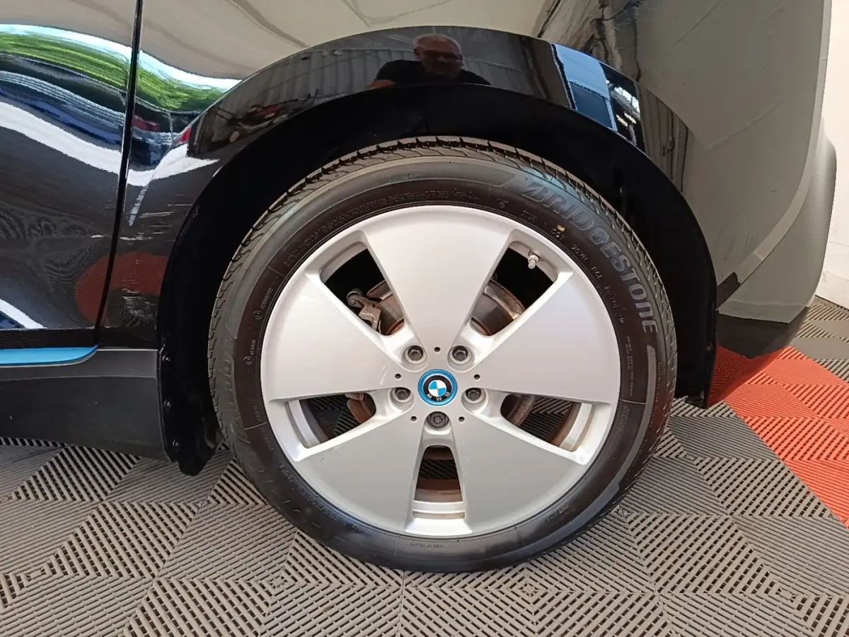 Gros plan sur la roue avant gauche d'une BMW i3 noire avec jante argentée et logo BMW au centre.