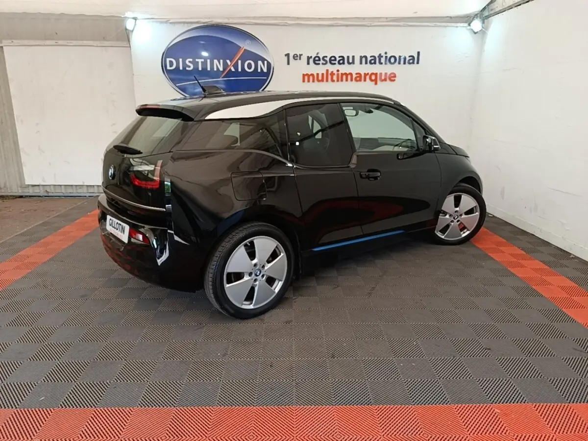 BMW i3 120 Ah Atelier noire vue de 3/4 arrière droit, dans un showroom avec sol gris et bandes rouges.