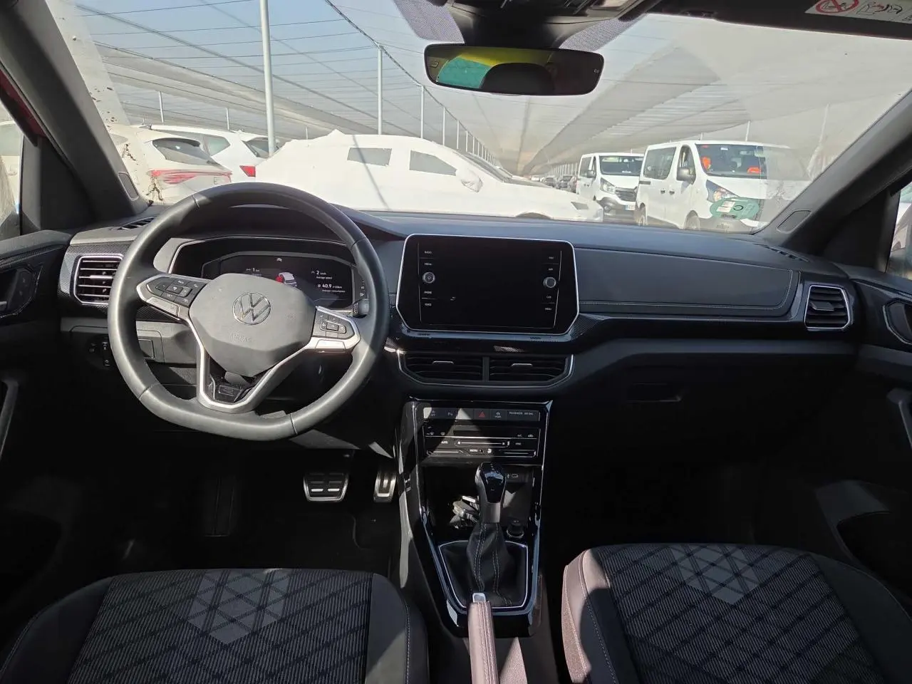 Vue intérieure avant du Volkswagen T-Cross 2025, tableau de bord noir avec volant multifonctions et écran tactile central.