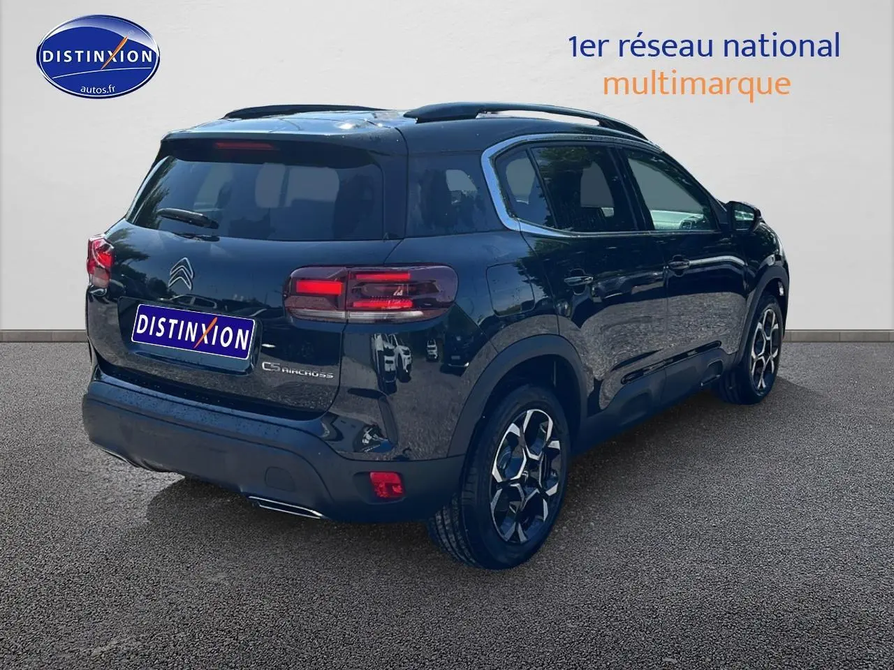 Vue 3/4 arrière droite d'un Citroën C5 Aircross noir avec toit bi-ton et jantes alu 18 pouces sur sol gris.