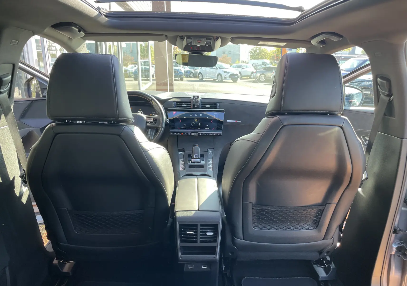Vue intérieure arrière du DS7 gris Artens, montrant les sièges avant en cuir noir et la console centrale avec écran tactile.