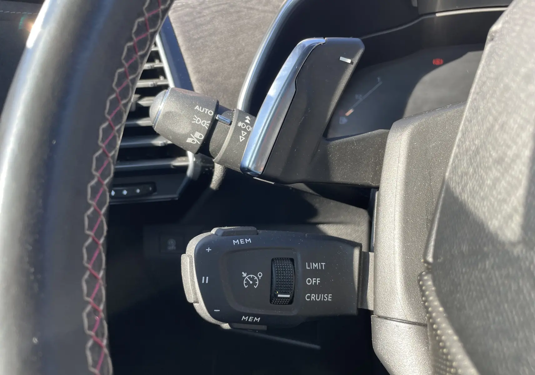 Gros plan sur les commandes de régulateur de vitesse et éclairage à gauche du volant du DS7 gris, intérieur noir.