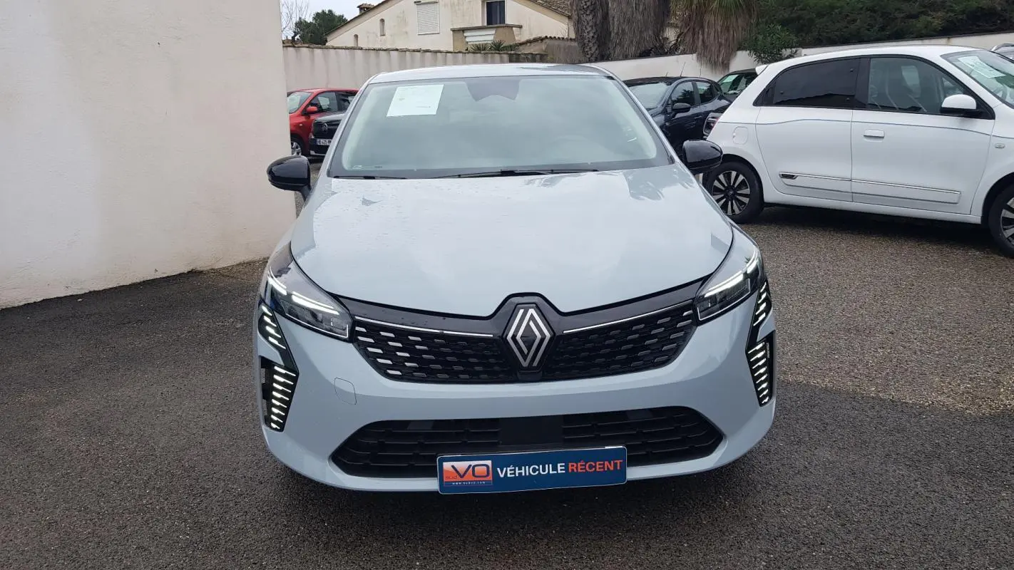 Vue de face d'une Renault Clio gris clair 2025 avec feux LED allumés et calandre noire distinctive.