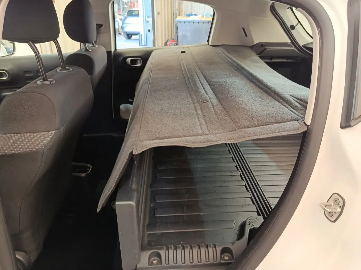 Vue intérieure côté droit du coffre ouvert d'une Citroën C3 blanche 2022 avec tapis de coffre relevé.
