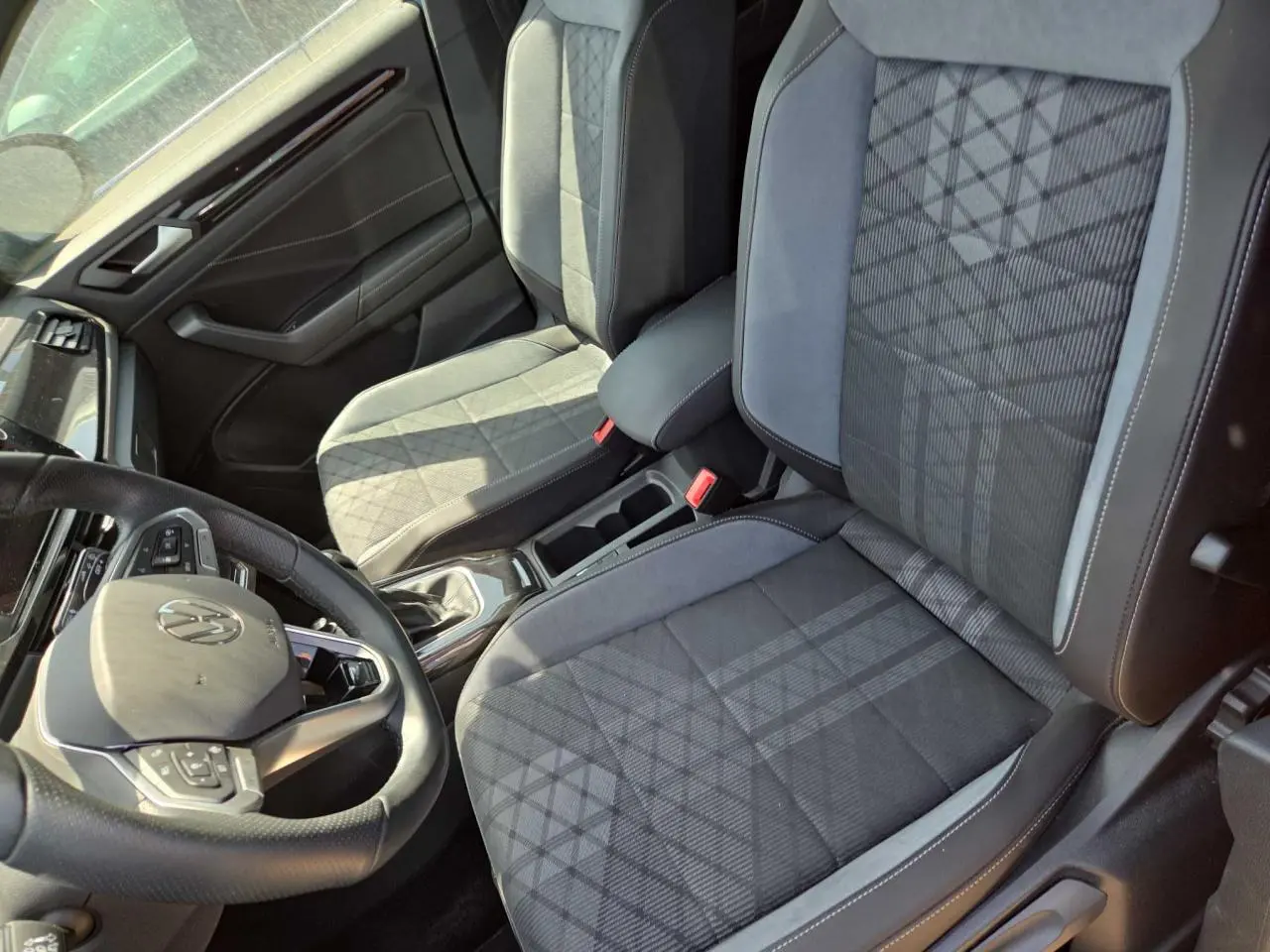 Vue intérieure côté conducteur du Volkswagen T-Roc 2025 noir métal, sièges tissu gris à motifs et volant multifonction cuir.