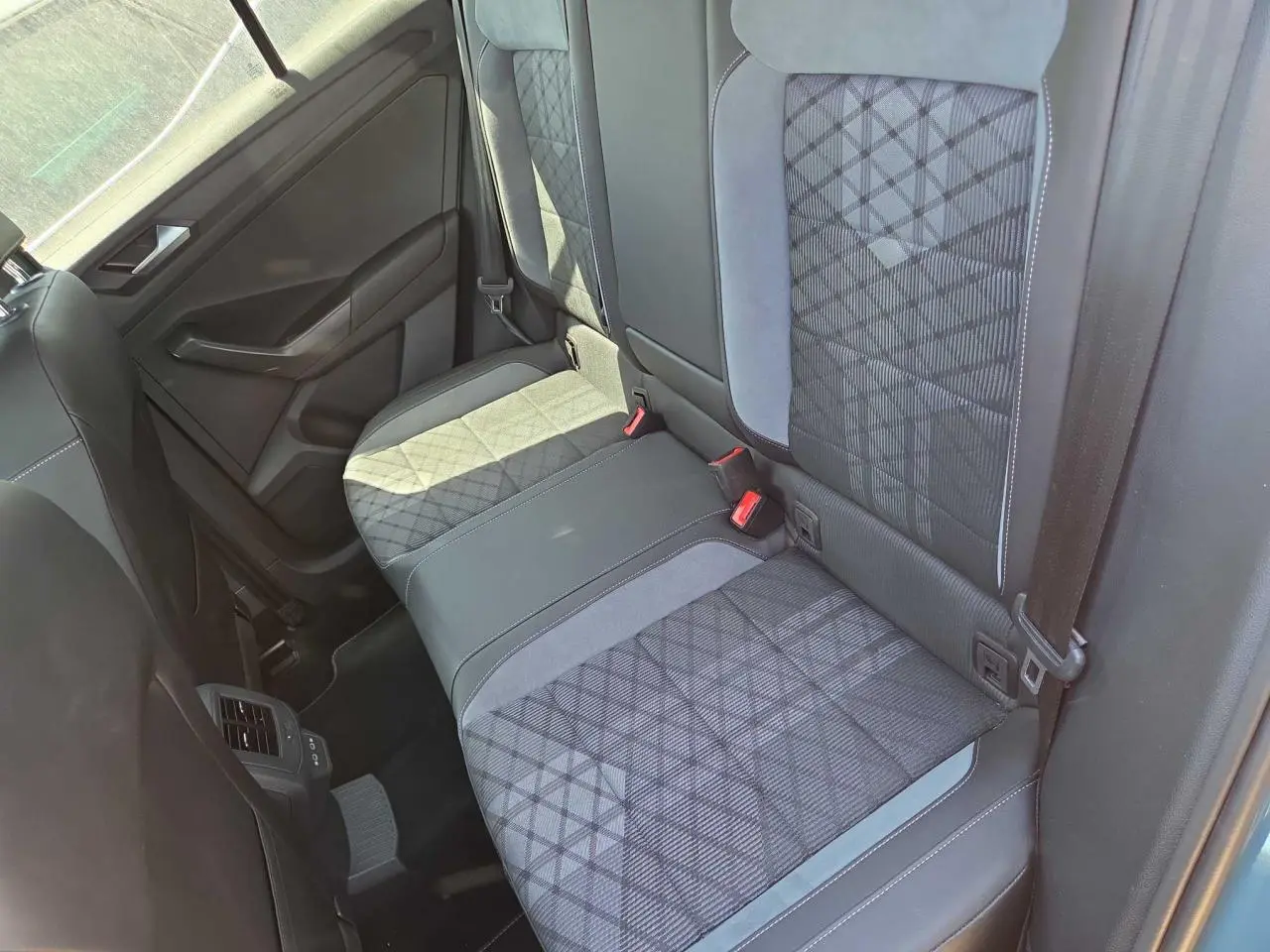 Vue intérieure de la banquette arrière du Volkswagen T-Roc 2025, tissu gris à motifs géométriques et ceintures visibles.