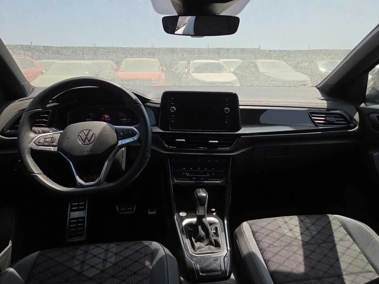 Vue intérieure avant du Volkswagen T-Roc noir métal 2025, avec volant multifonction et écran tactile central.
