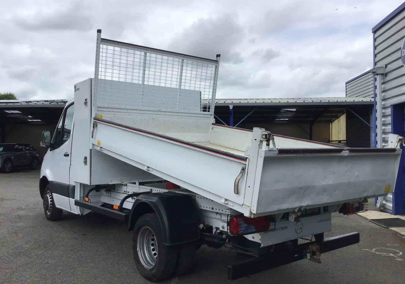 Mercedes Sprinter blanc 514 CDI en vue 3/4 arrière droit, avec benne basculante et coffre latéral visible.