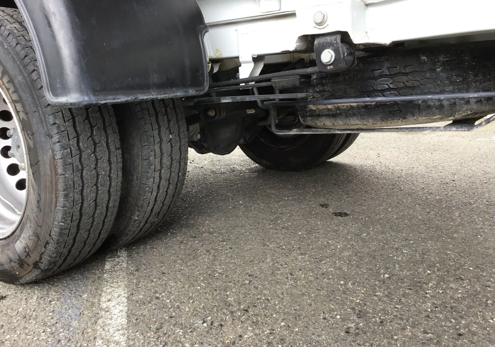 Gros plan sur les roues jumelées arrière gauche du Mercedes Sprinter blanc avec benne et coffre, vue sous le châssis.