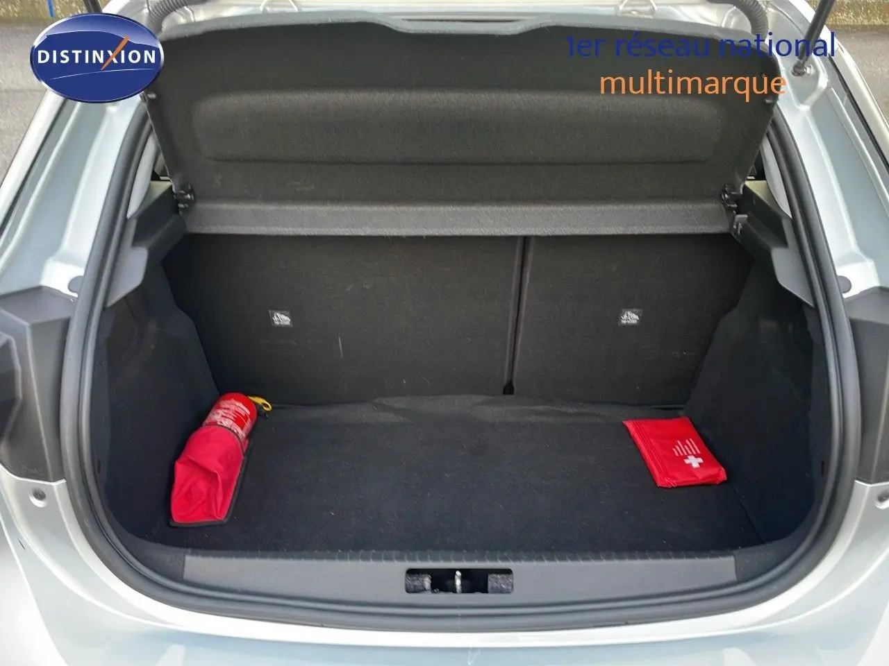 Coffre ouvert vu de l'arrière d'une Opel Corsa gris kristall metal, avec trousse de secours et extincteur rouge visibles.