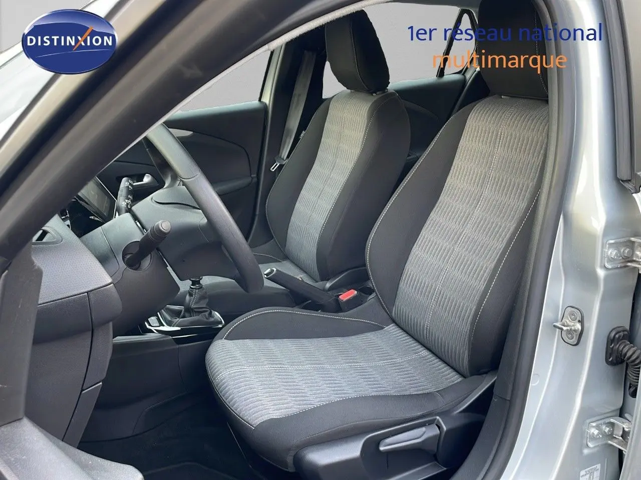 Vue intérieure côté conducteur de l’Opel Corsa gris kristall metal, montrant les sièges tissu gris et noir et la boîte manuelle.
