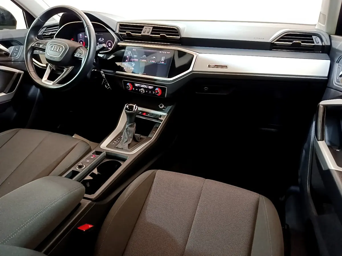 Intérieur de l'Audi Q3 35 TDI 2021 vu côté conducteur, tableau de bord noir avec écran tactile central lumineux.