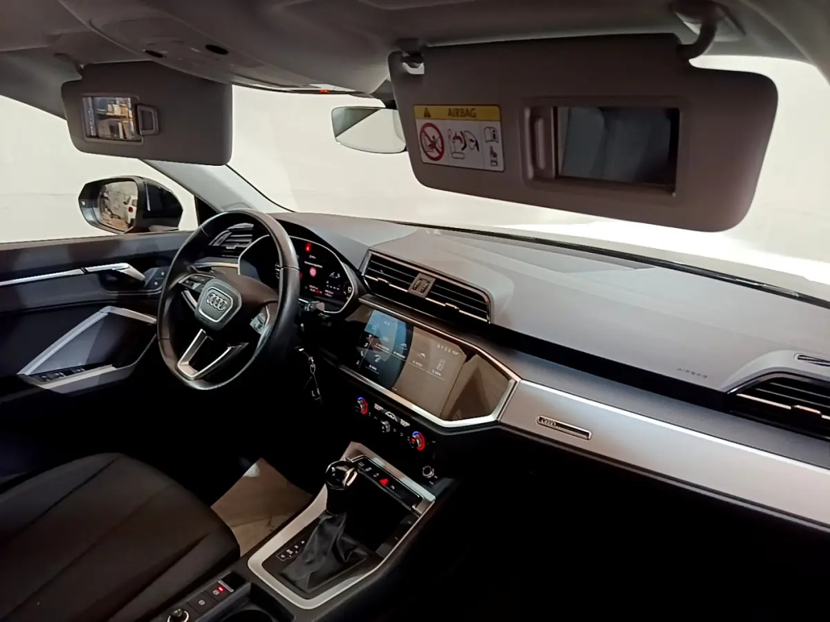 Intérieur de l'Audi Q3 35 TDI 2021 vu côté conducteur, tableau de bord moderne avec écran tactile et volant cuir noir.