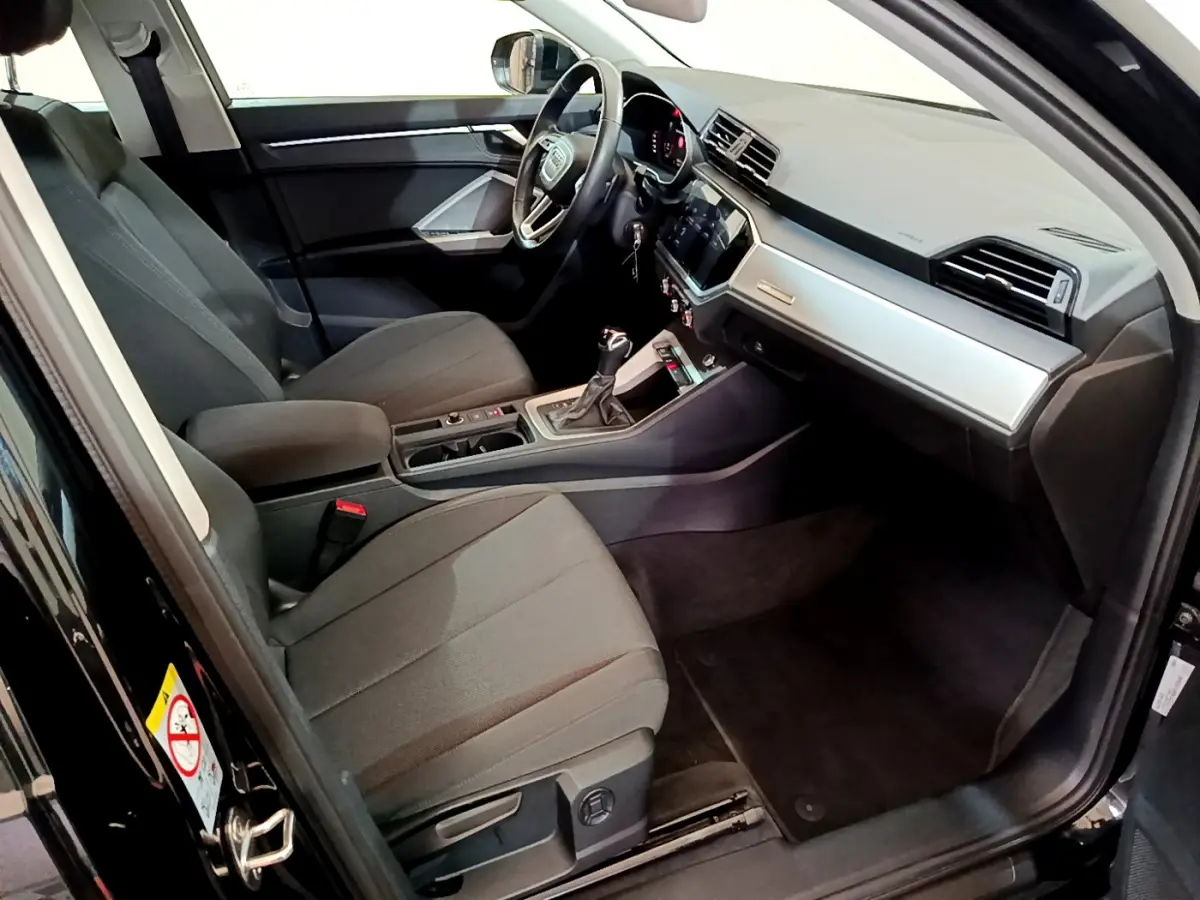 Intérieur côté conducteur d’un Audi Q3 noir 2021, montrant sièges tissu gris et tableau de bord moderne avec écran tactile.