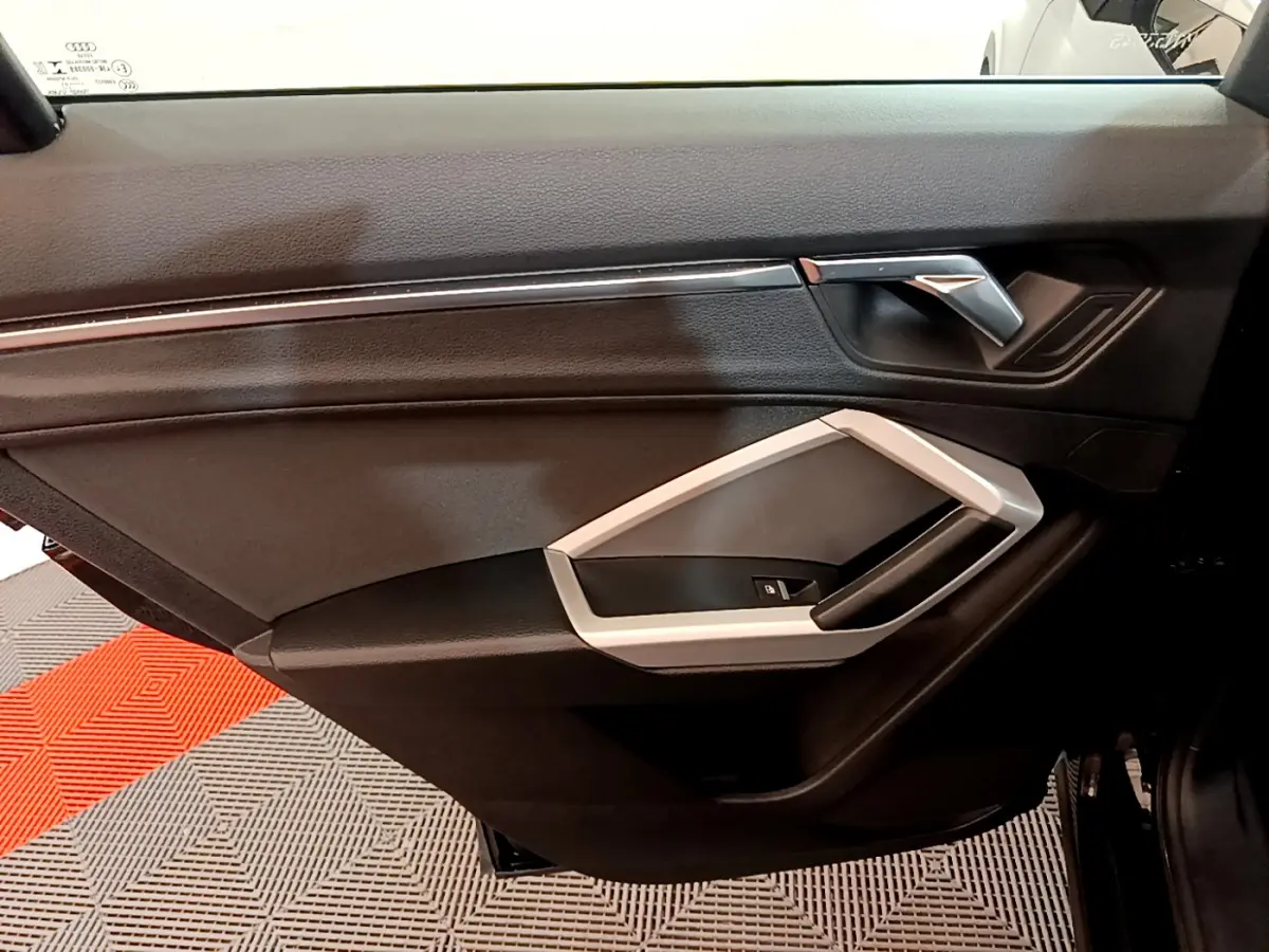 Gros plan sur la porte intérieure côté gauche de l'Audi Q3 noir, avec poignée argentée et bouton de verrouillage.
