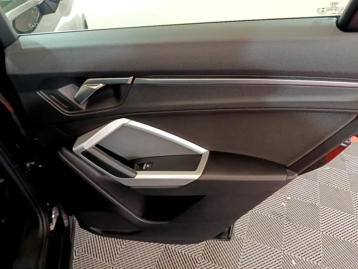 Vue rapprochée de la porte intérieure côté droit noire de l'Audi Q3 35 TDI 2021 avec poignée argentée.