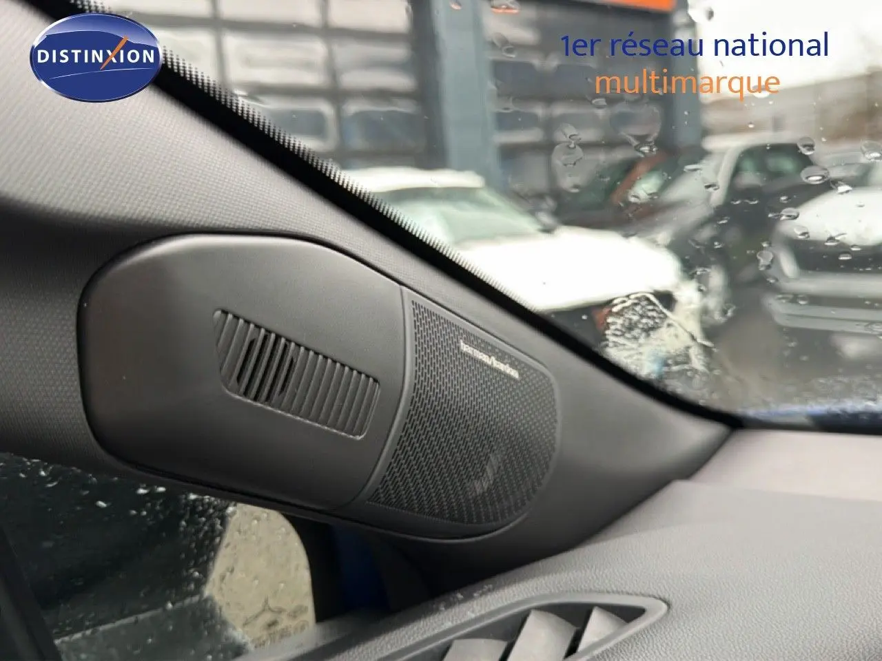 Gros plan sur l'enceinte Harman Kardon côté gauche du tableau de bord d'un Renault Captur bleu Iron Metal avec toit noir.