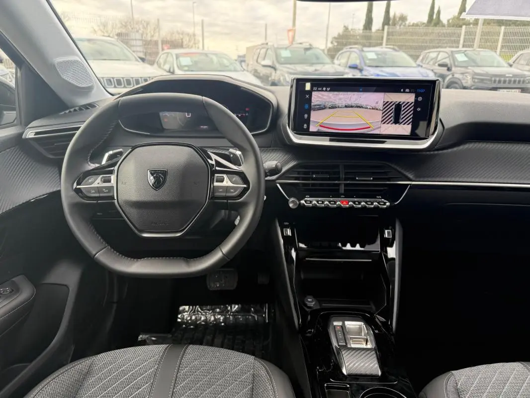 Vue intérieure avant du Peugeot 208 Hybrid 145 Allure 2025, volant compact, écran tactile avec caméra de recul, finition noire et grise.